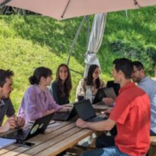 personnes autour d'une table dehors en été en train de travailler sur leur ordinateur